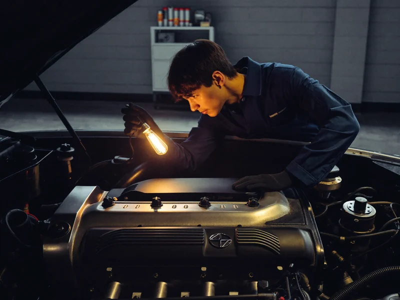 Ilustrație: mecanic cu mănuși care inspectează compartimentul motor cu o lampă
